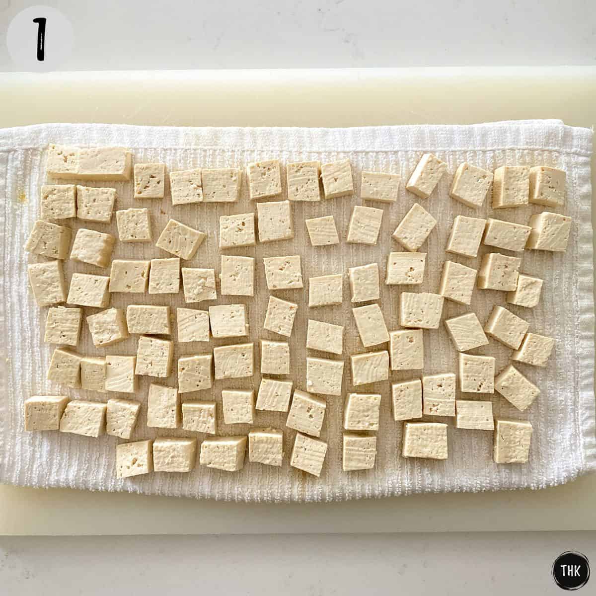 Tofu cubes on dish towel on top of cutting board.
