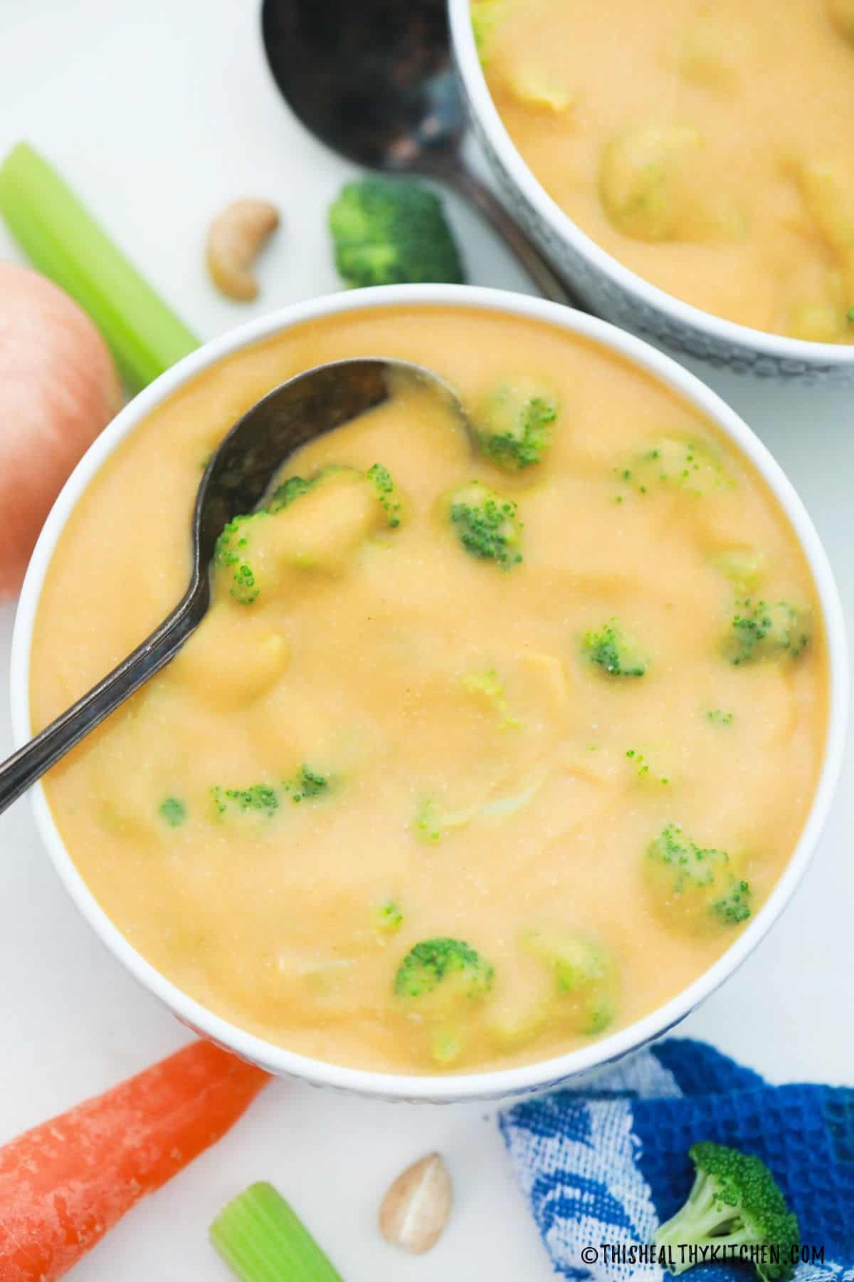 Two bowls of vegan cheesy broccoli soup with spoon inside one.