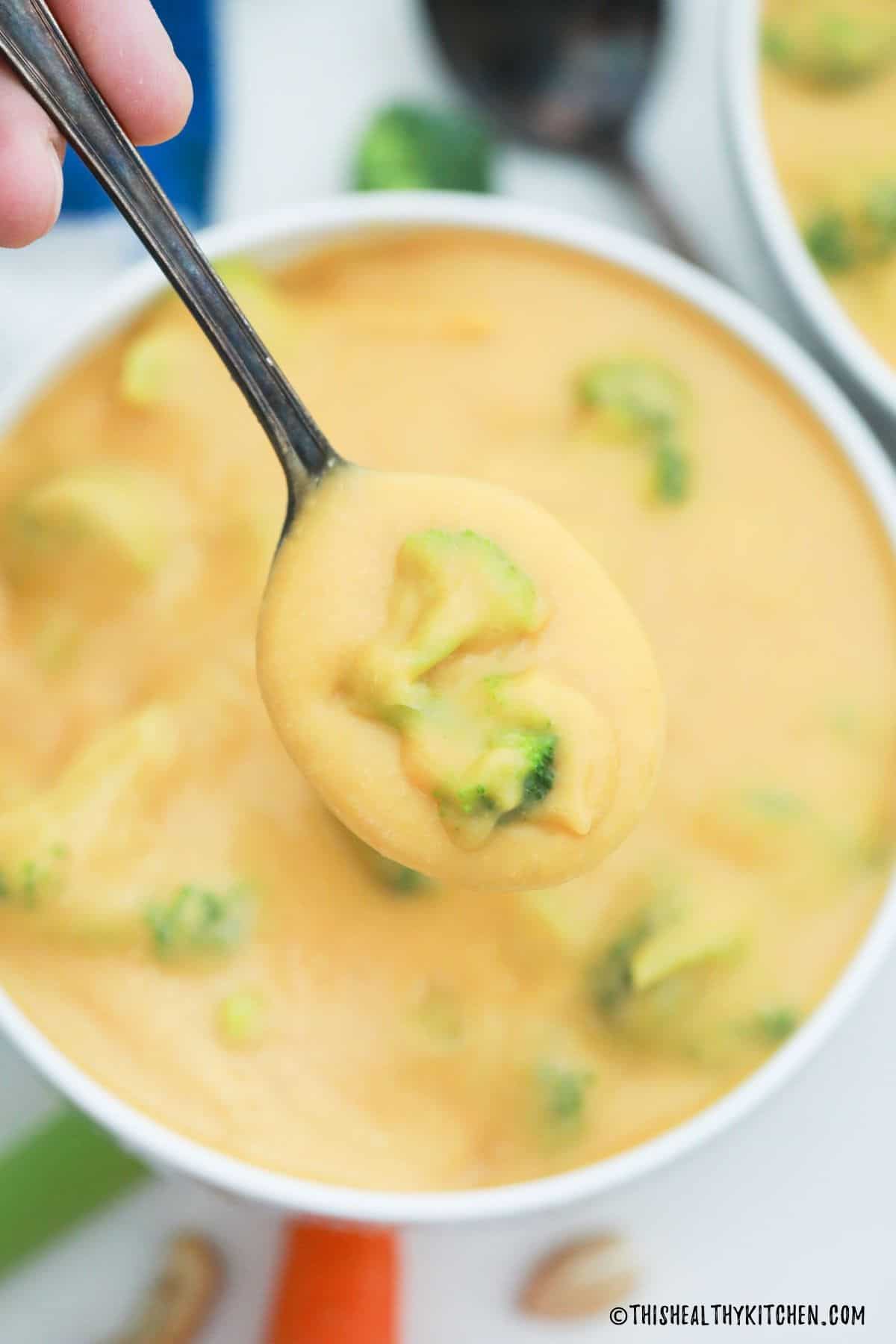 Spoonful of broccoli cheddar soup being held above bowl.