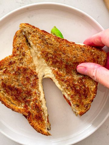 Hand pulling apart vegan grilled cheese sliced in half on plate.