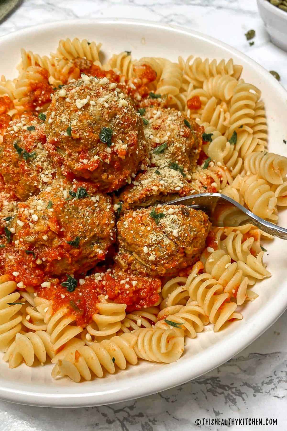 Fork cutting through a meatball resting on plate of pasta.