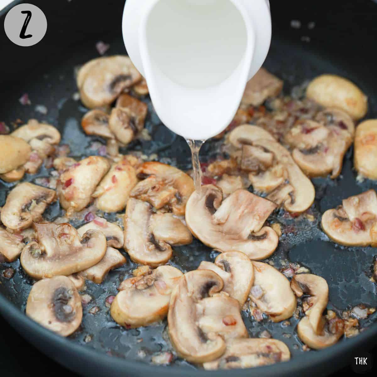 Vodka being poured into skillet of sauted mushrooms and shallots.