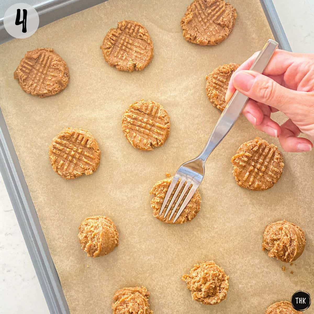 Fork pressing into almond butter cookies to make crisscross pattern.