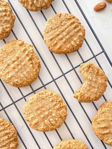 Almond butter cookies on cooling rack with bite taken from one.