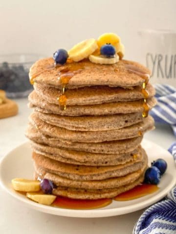 Stack of buckwheat pancakes on plate with banana and blueberries on top.