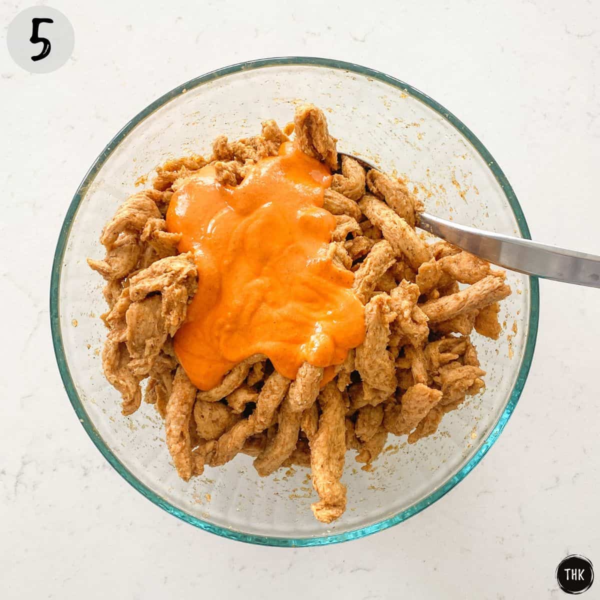 Buffalo sauce sitting on top of bowl of soy curls.
