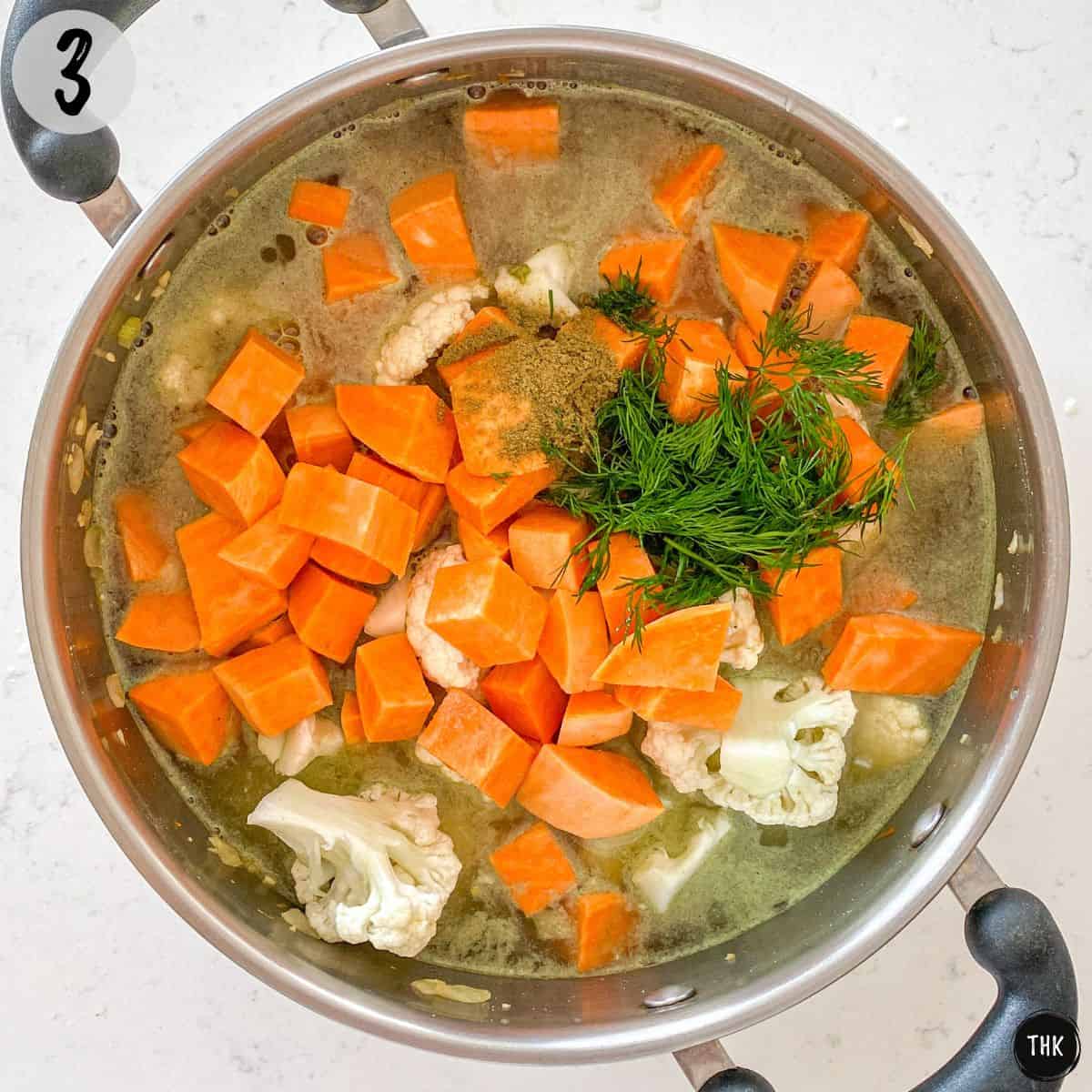 Soup pot with broth, cubed sweet potato, cauliflower, carrots, and spices inside.