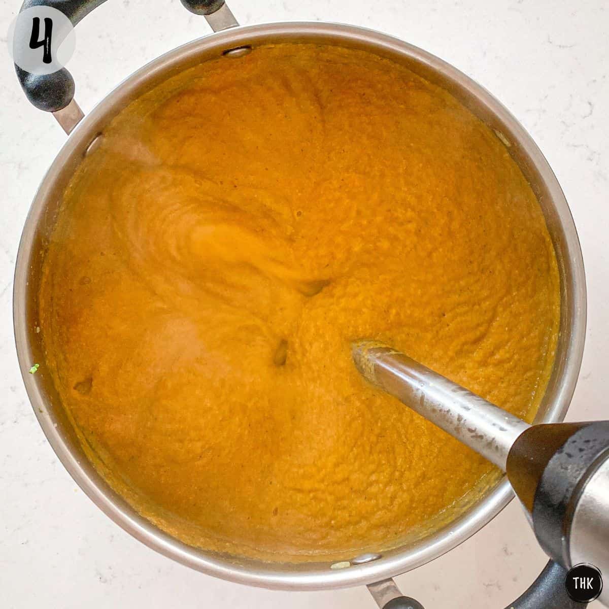 Hand blender pureeing large pot of orange coloured soup.