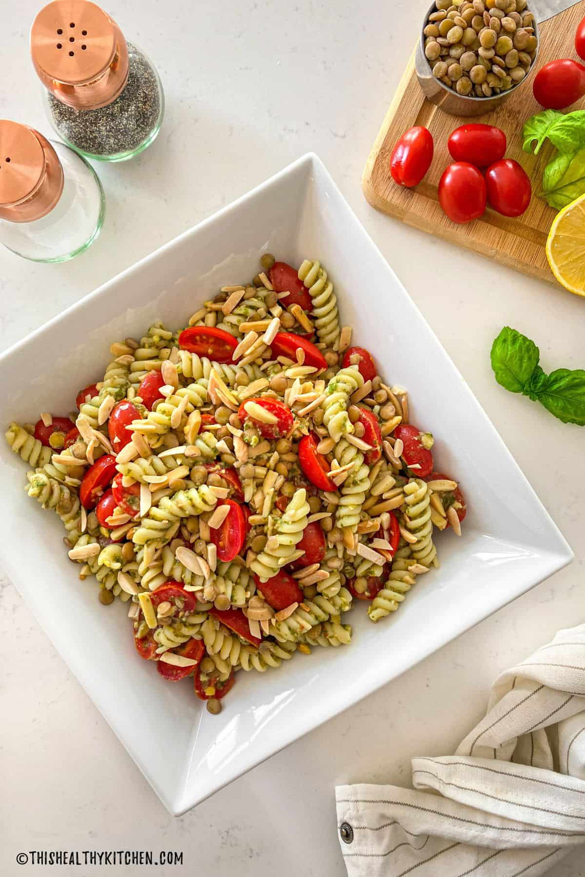 White serving dish with pasta salad with tomatoes, basil, and slivered almonds.