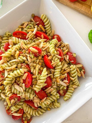 White serving dish filled with rotini pasta, cherry tomatoes, lentils and slivered almonds.