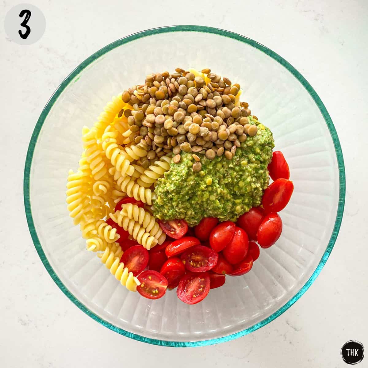 Large bowl with cooked pasta, lentils, pesto, and cherry tomatoes inside.