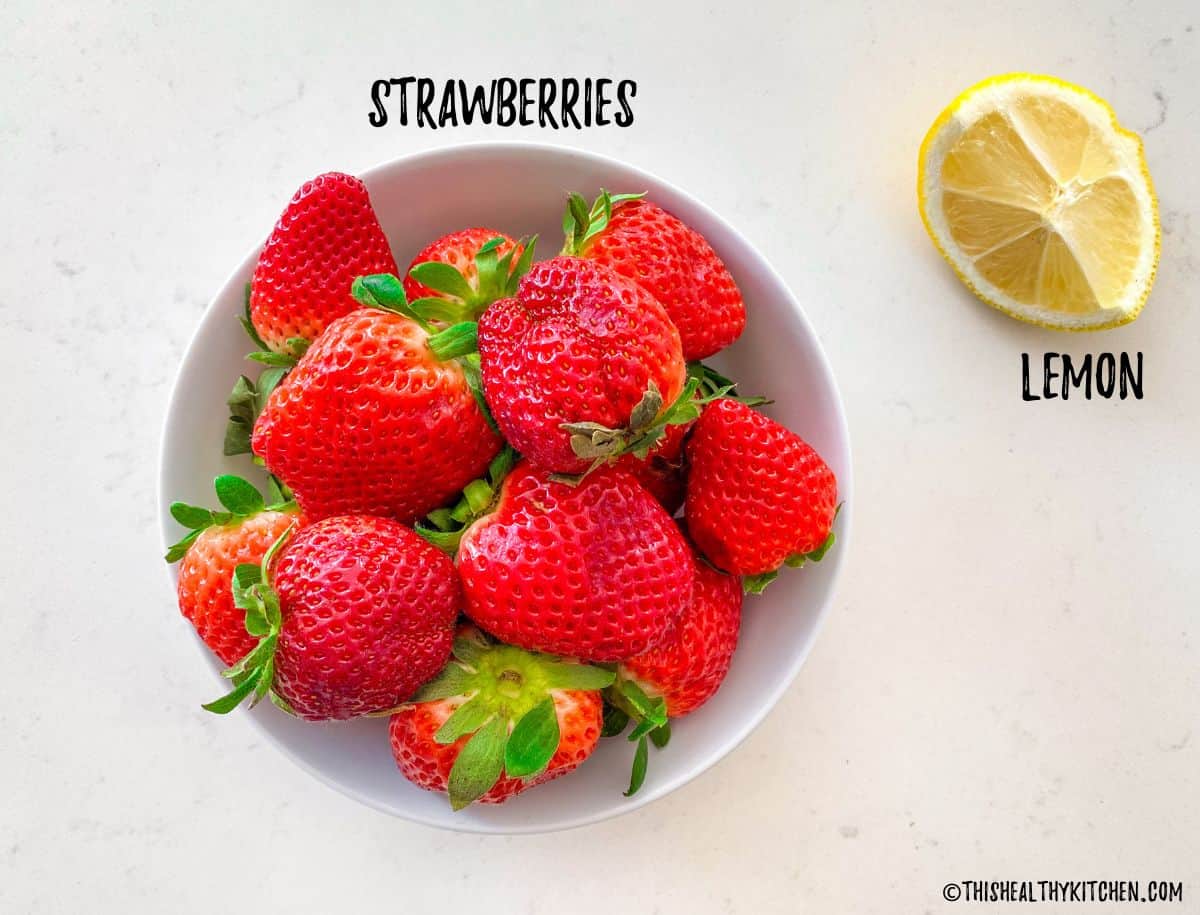 Bowl of strawberries and wedge of lemon beside it.