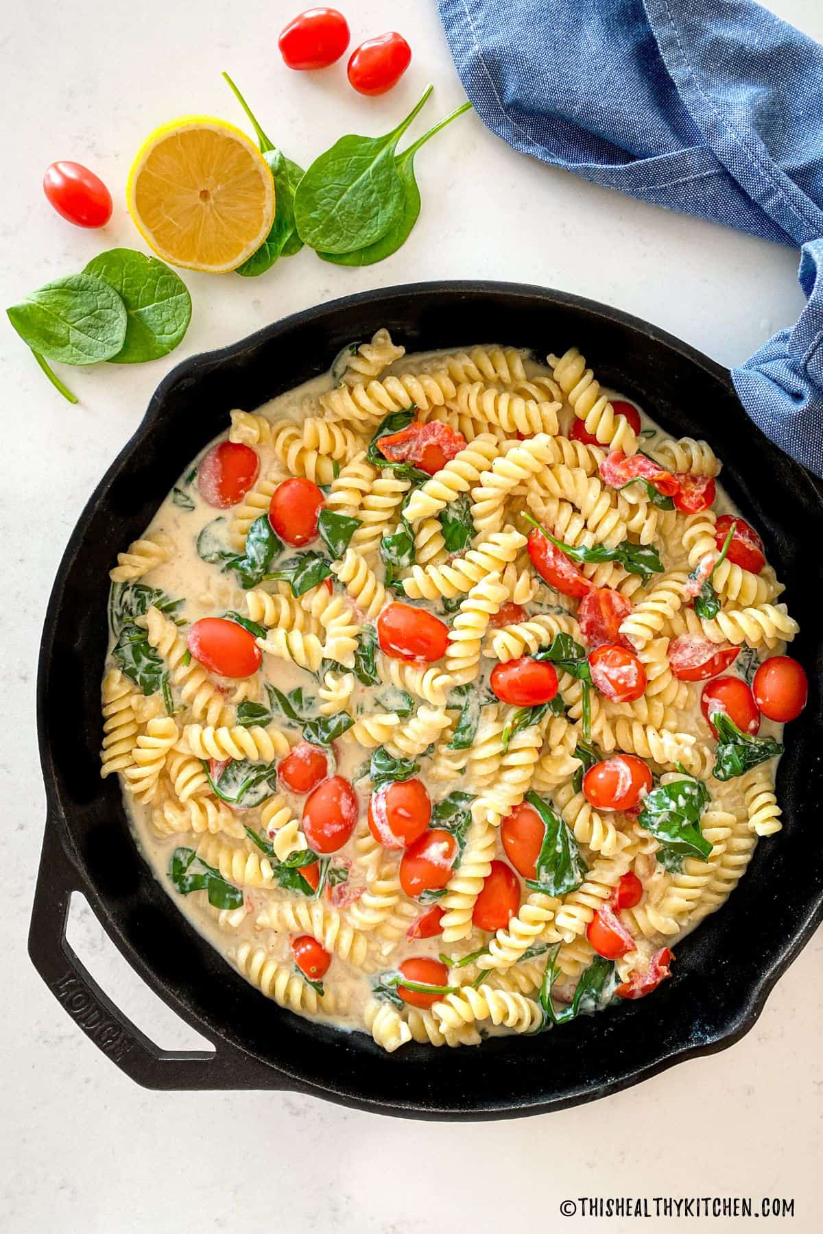 Cast iron pan with rotini pasta, cherry tomatoes and spinach in a white sauce.