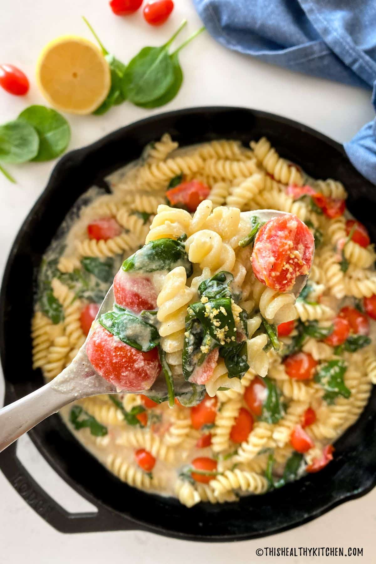 Spoonful of pasta with tomatoes and spinach being held over pan.