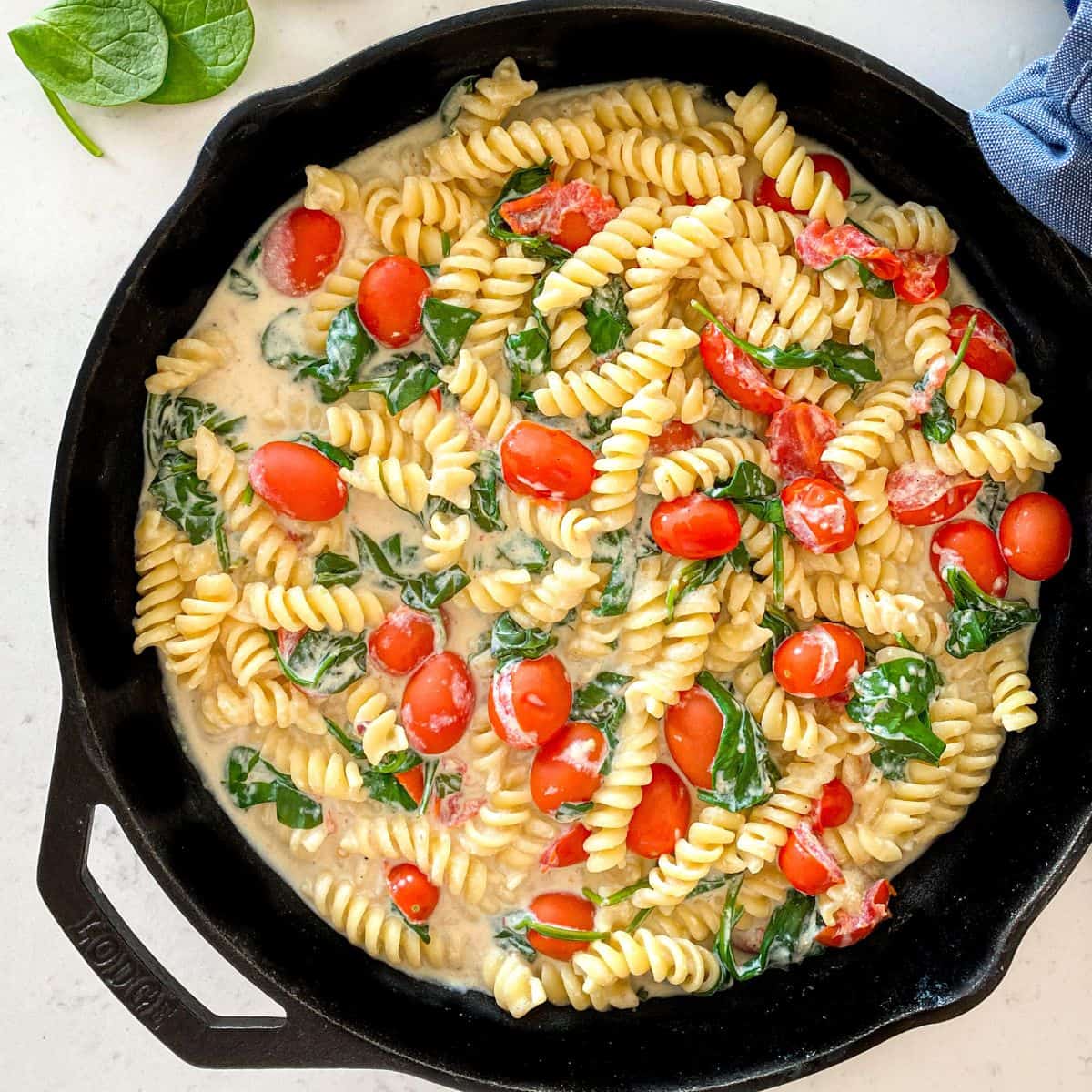 Cast iron pan with rotini pasta, cherry tomatoes and spinach in a white sauce.