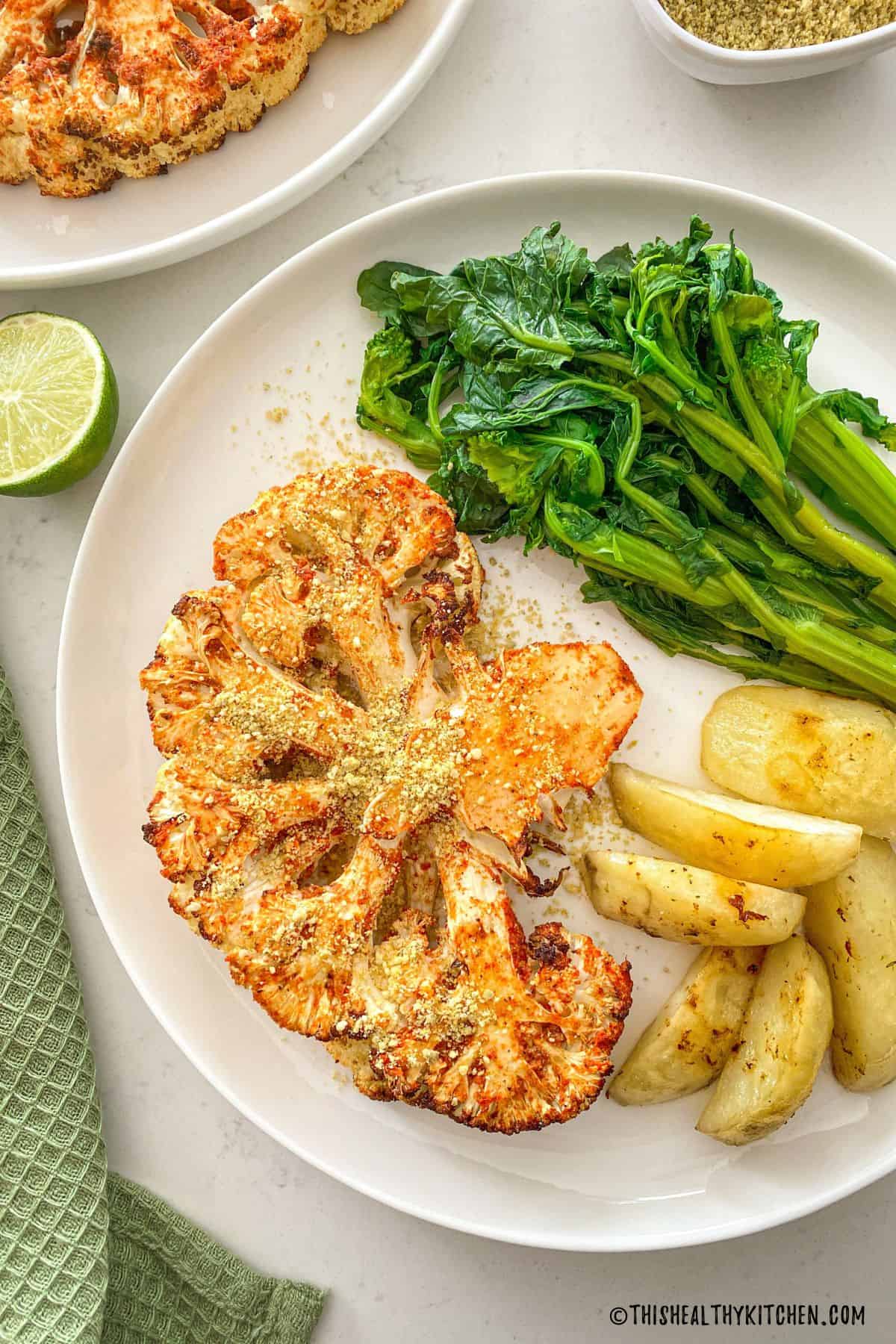 Air fried cauliflower steak on plate with potato wedges and rapini.