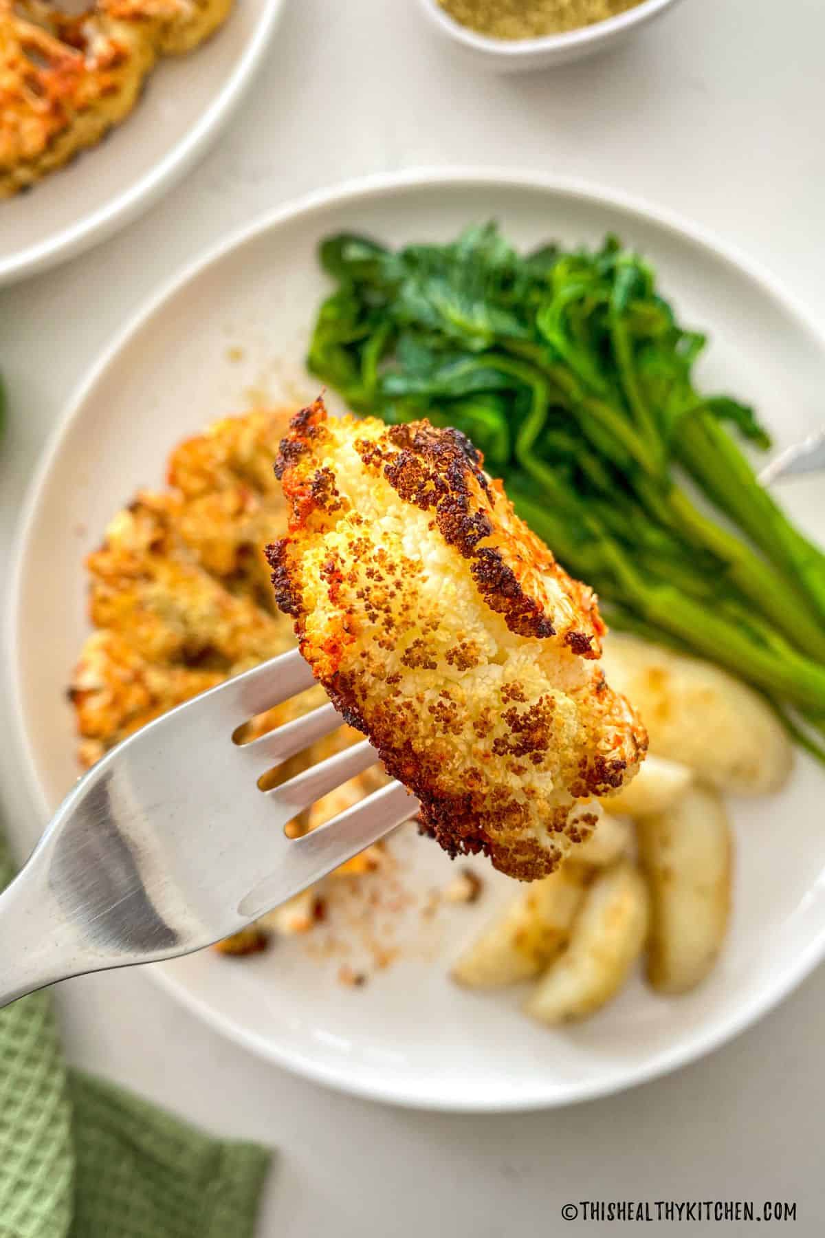 Bite of cauliflower steak on fork with remaining in plate below.