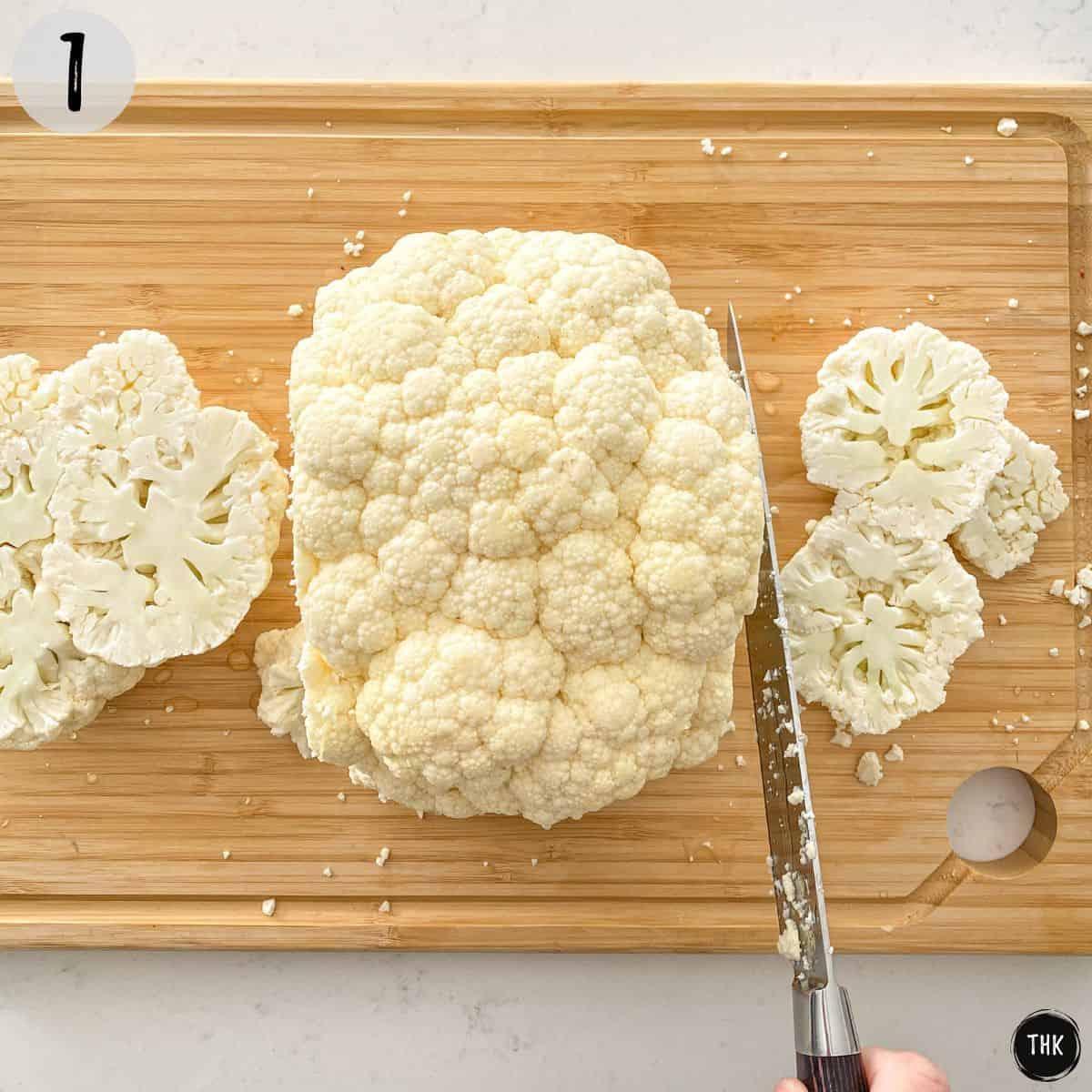 Cauliflower head on cutting board being sliced.