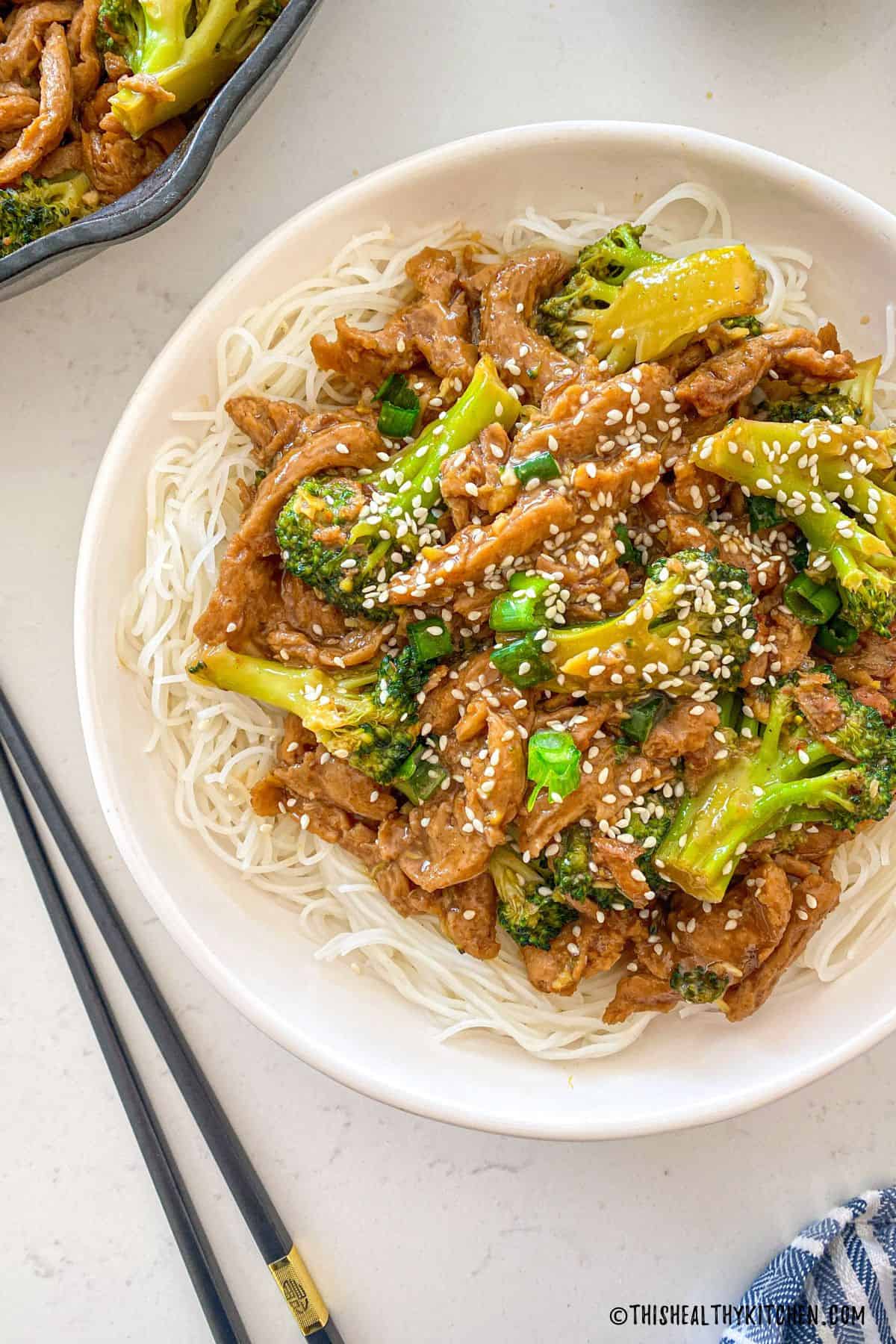 White dish with noodles and vegan beef and broccoli on top.
