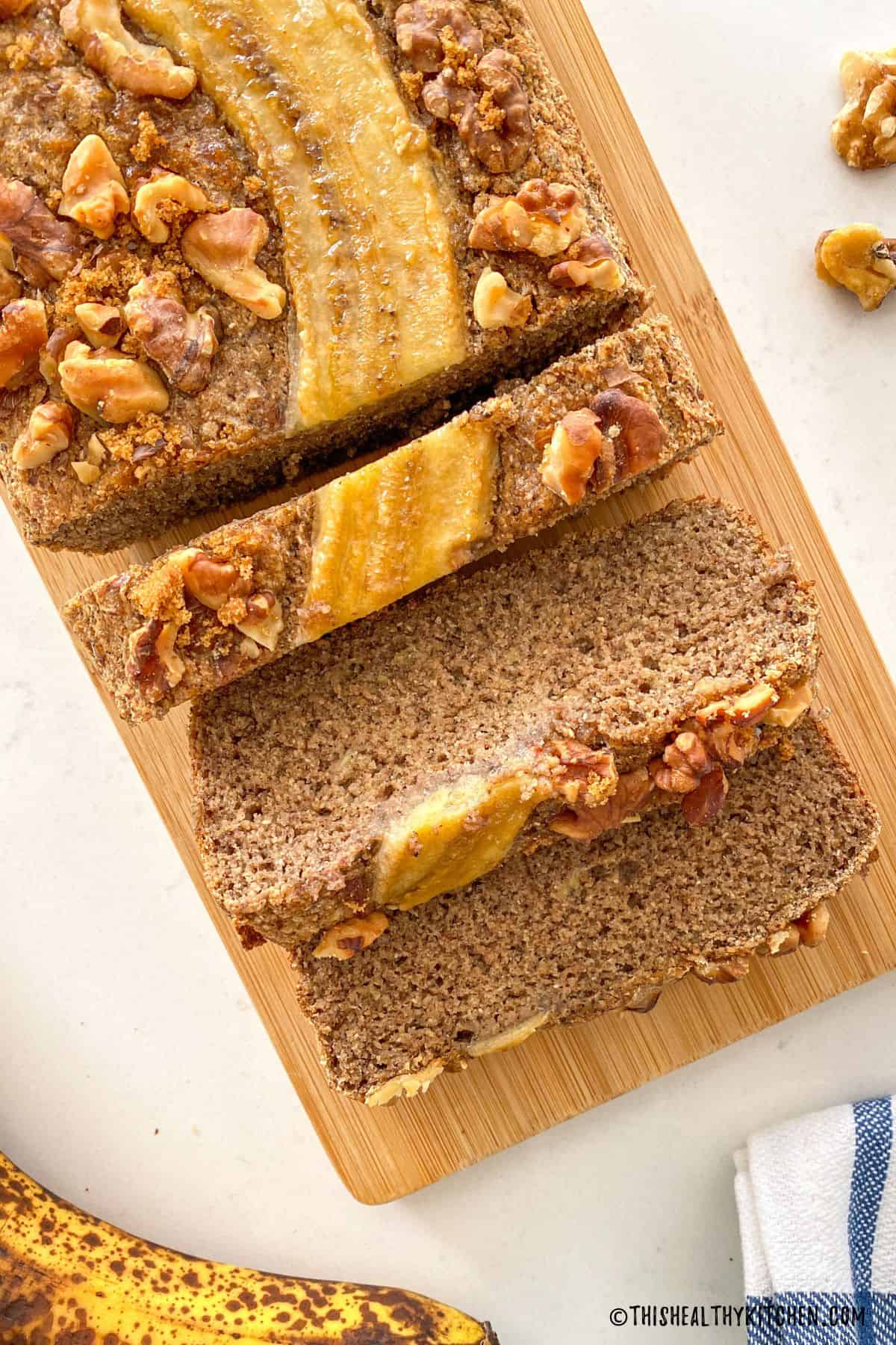 Banana bread with walnuts on top sliced on cutting board.
