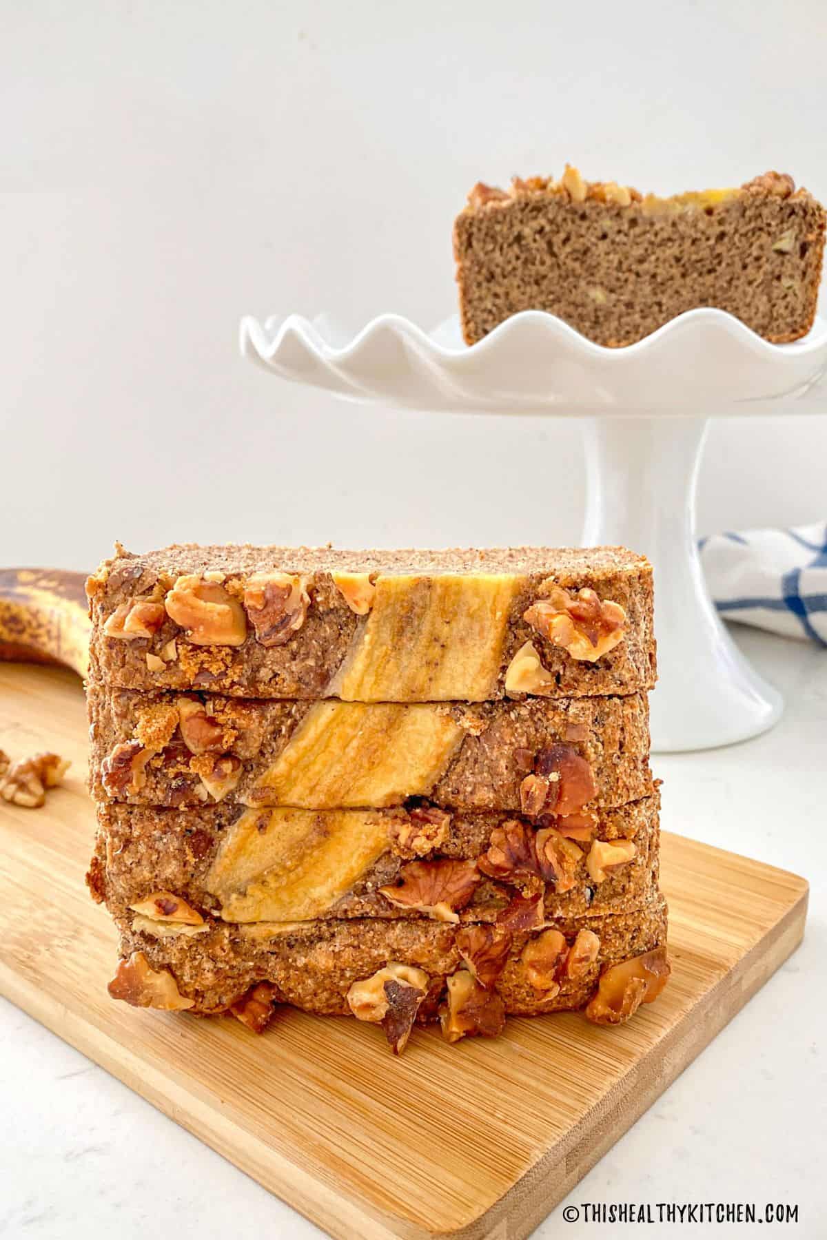 Four slices of banana bread stacked vertically on cutting board.