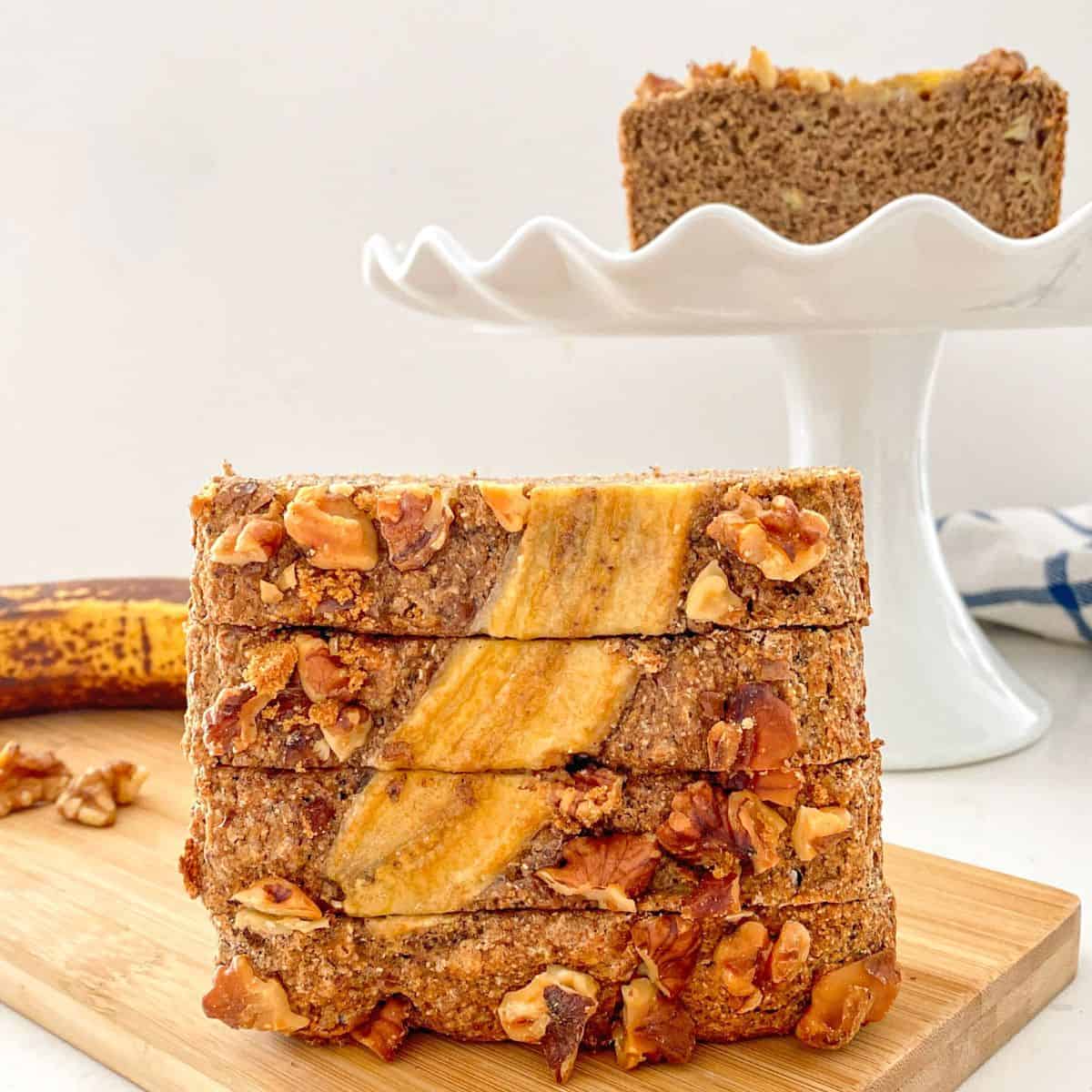 Four slices of banana bread stacked vertically on cutting board.