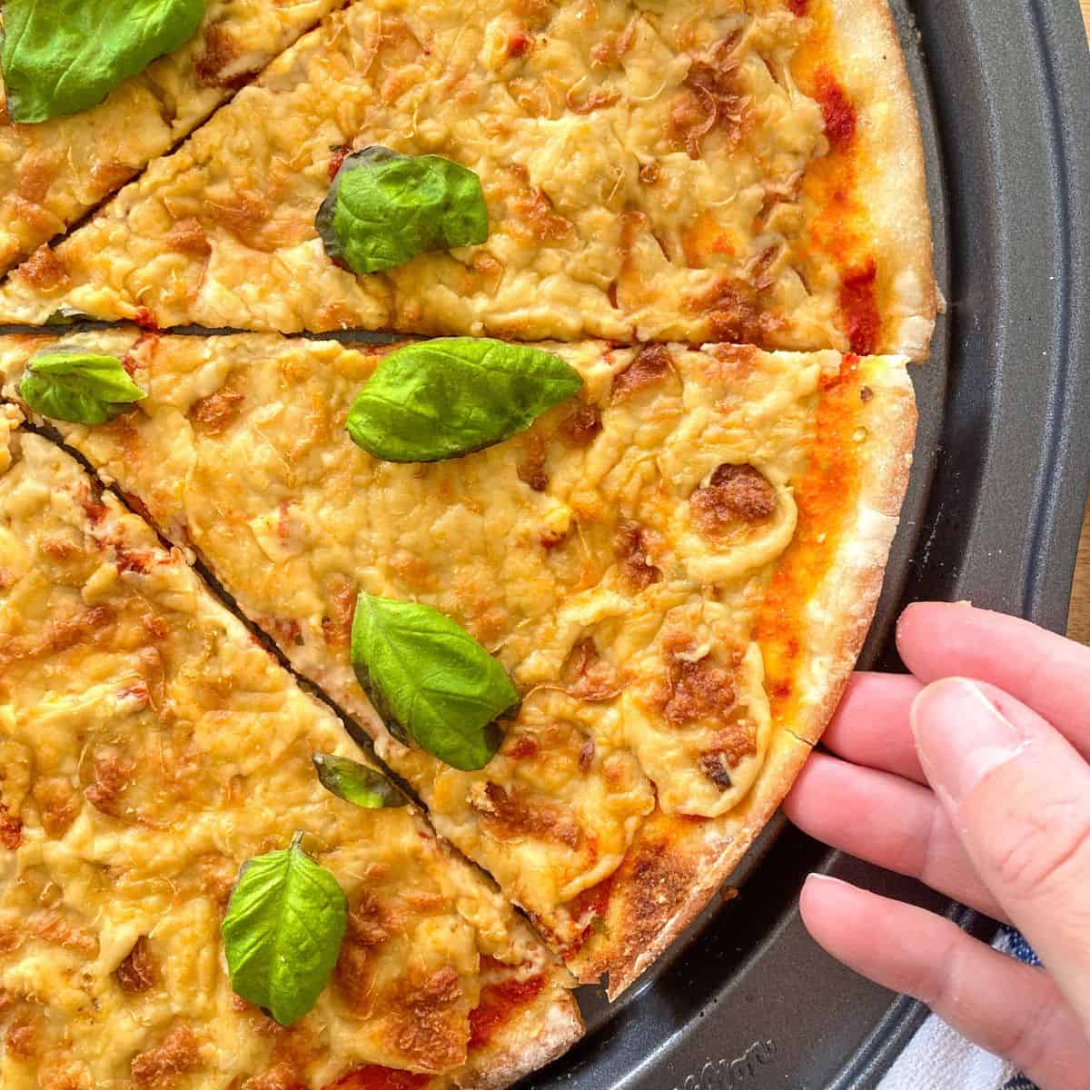 Hand reaching for slice of cheese pizza from pan.