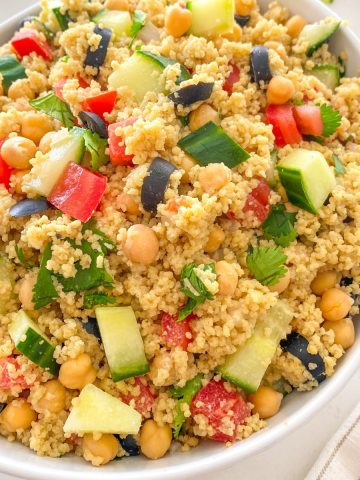 Large bowl of couscous, tomato, cucumber, olives, chickpeas and cilantro.