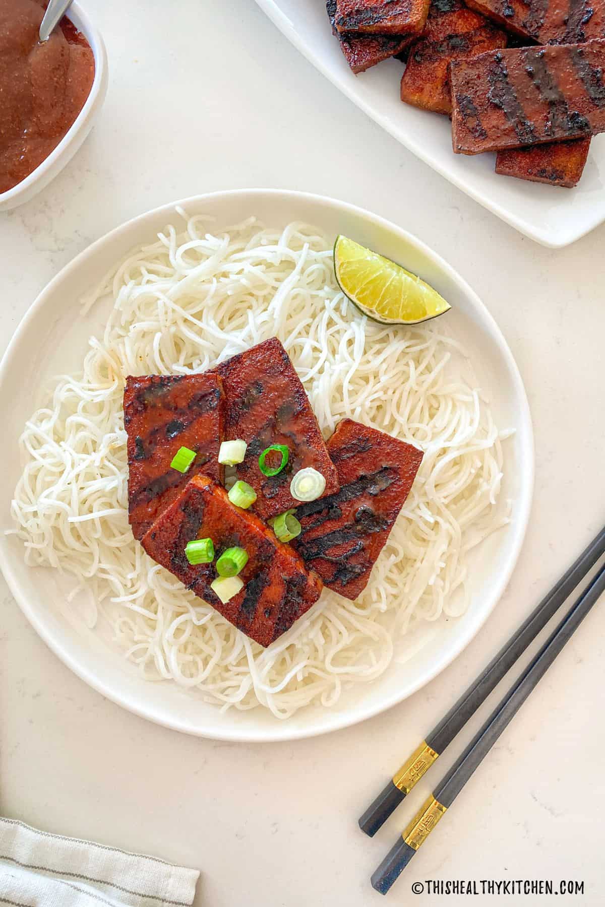Smoked tofu slices on top of noodles in white plate.