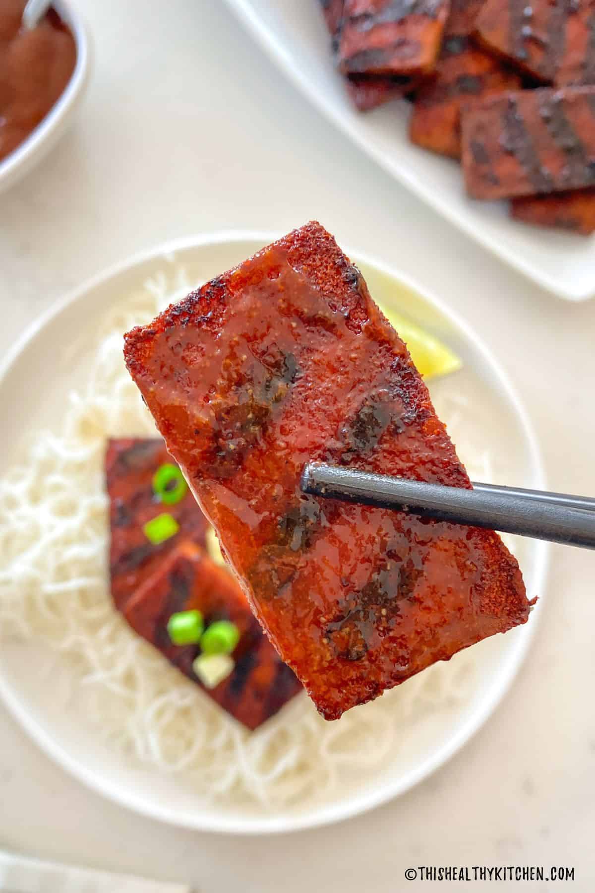 Chopsticks holding up one slice of smoked tofu.