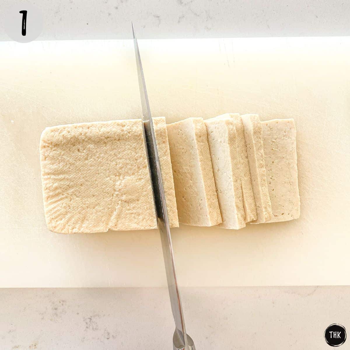 Tofu being sliced on cutting board.