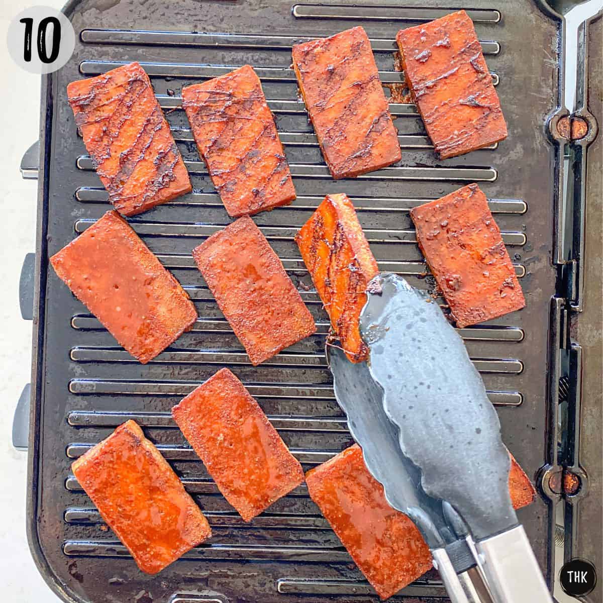 Smoked tofu slices being flipped on grill.