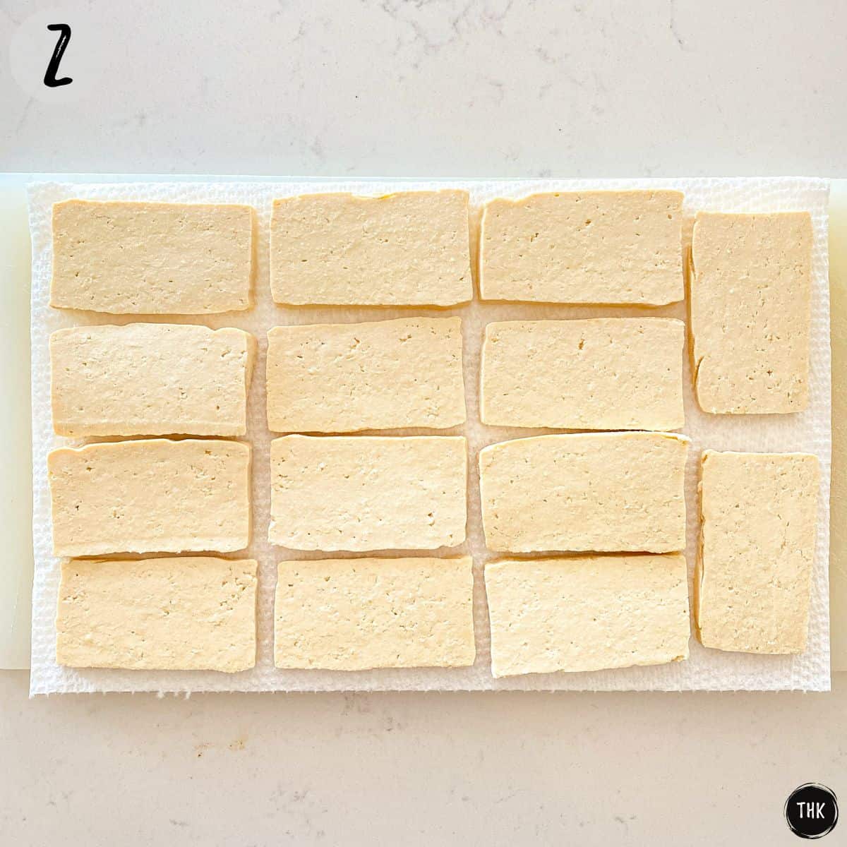Tofu slices arranged in single layer on paper towel and cutting board.
