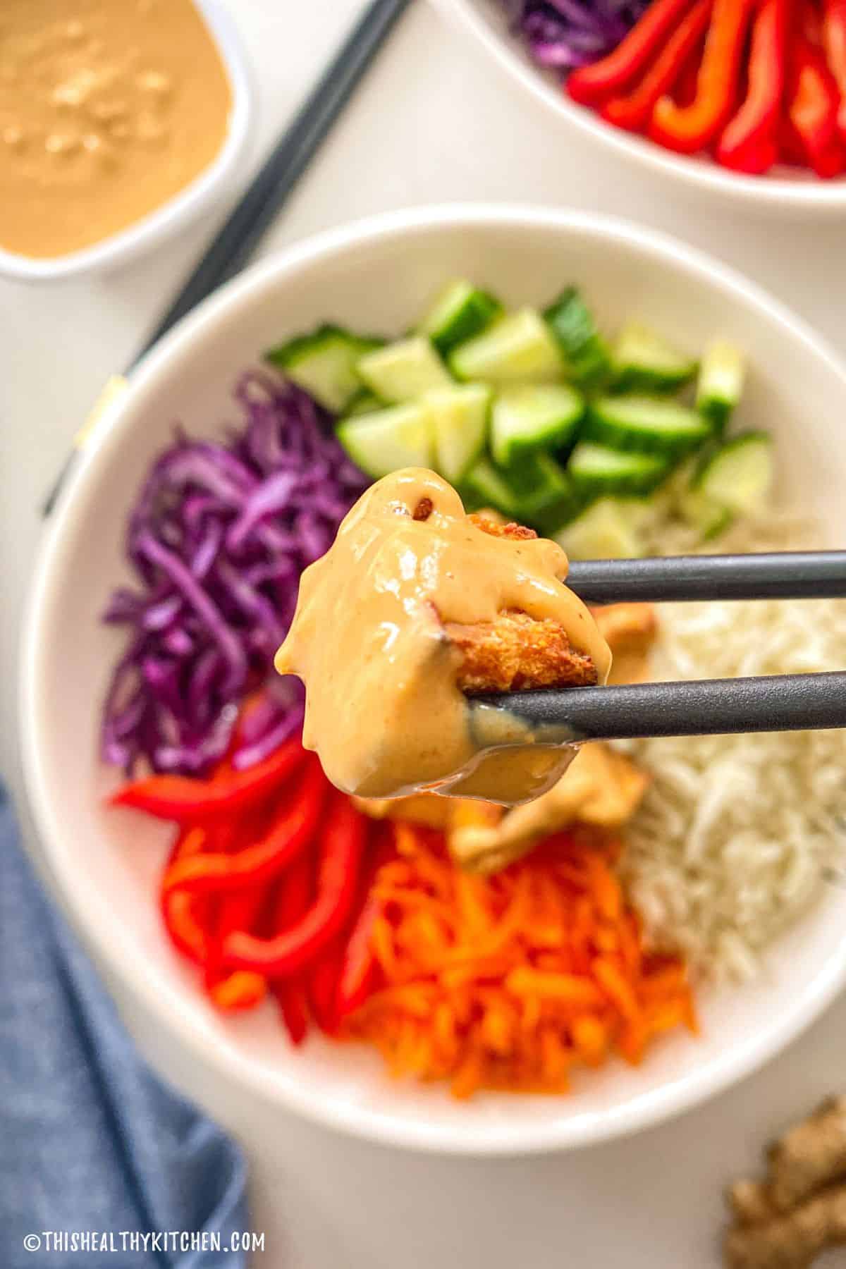 Chopsticks holding up tofu square with peanut sauce on top.