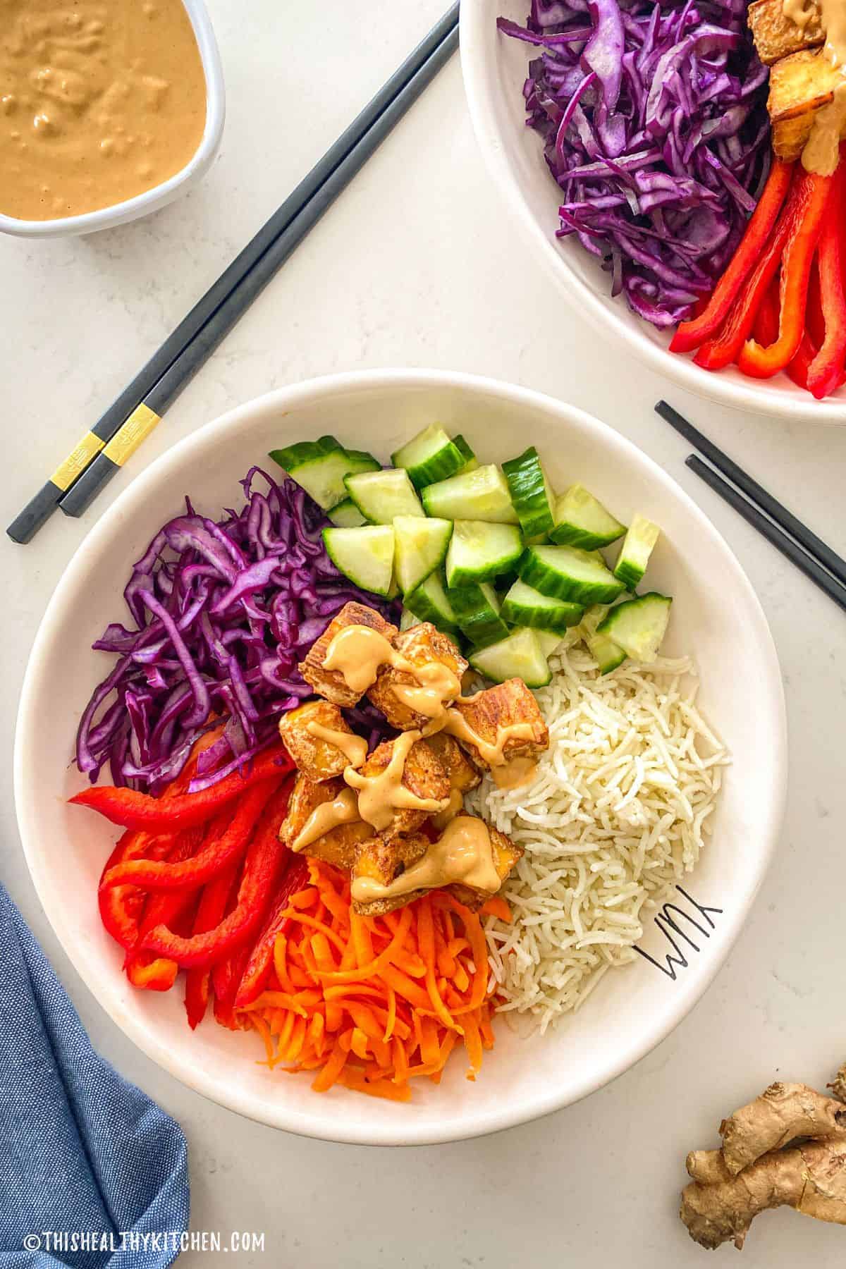 Two tofu buddha bowls with tofu, rice, cucumber, carrots, peppers and cabbage.