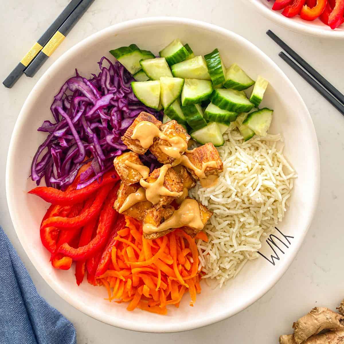 Bowl with peanut tofu, cucumber, rice, red pepper, shredded carrots and purple cabbage.