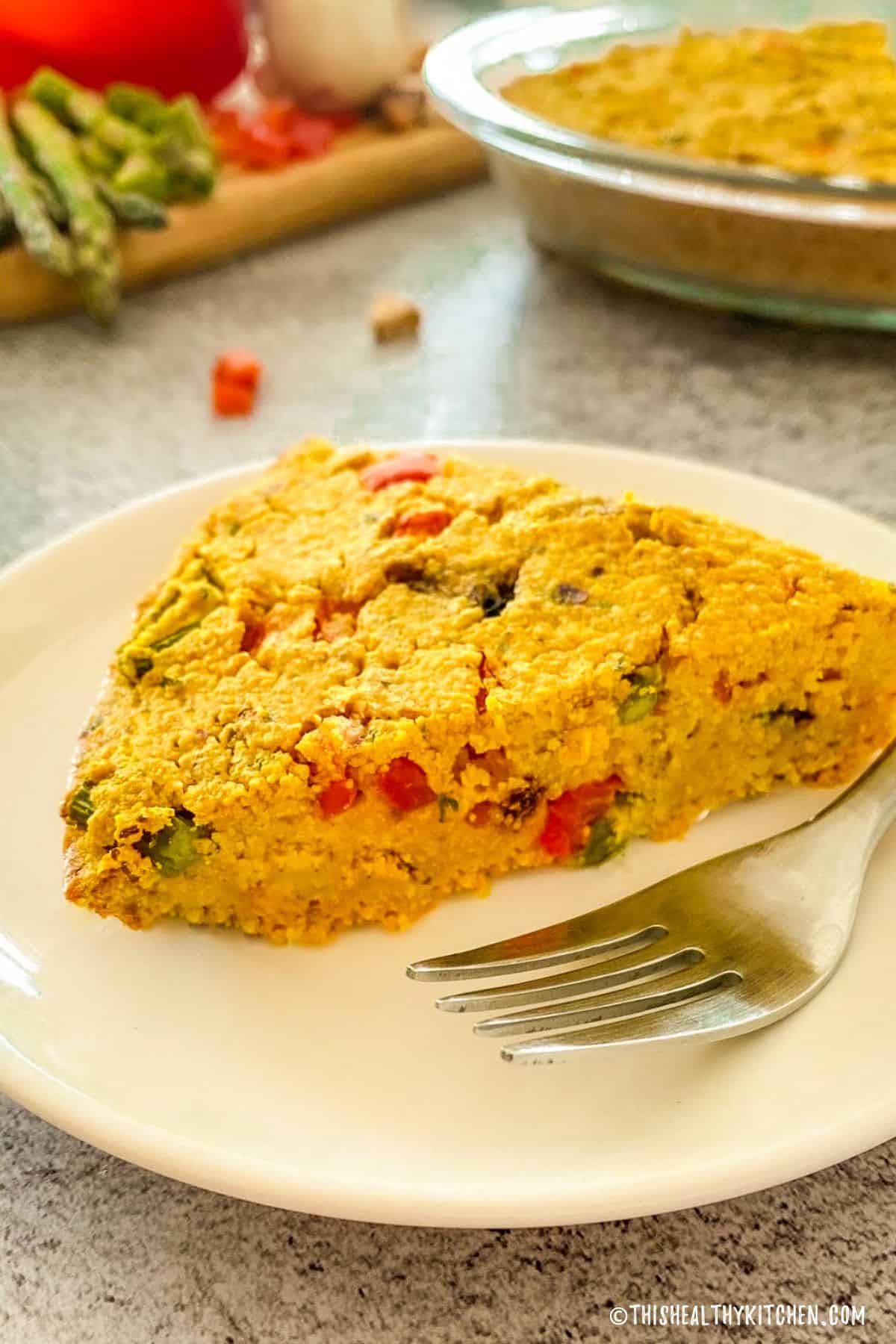 Slice of vegan frittata in plate with fork beside it.