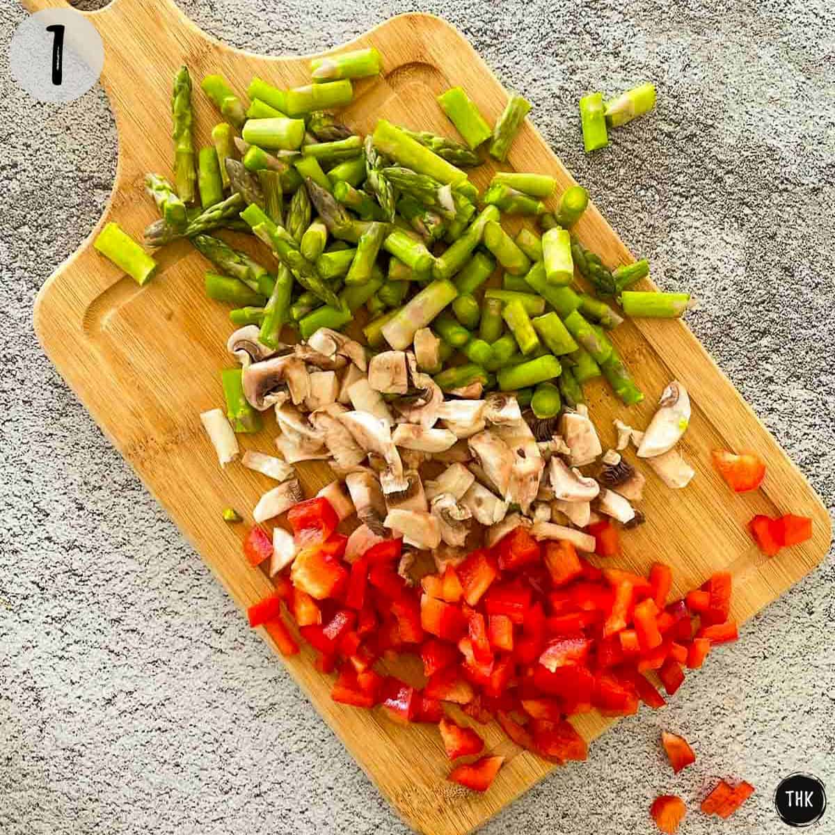 Cutting board with chopped asparagus, mushrooms, and peppers.