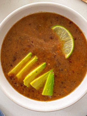 Bowl of black bean soup with avocado and lime on top.