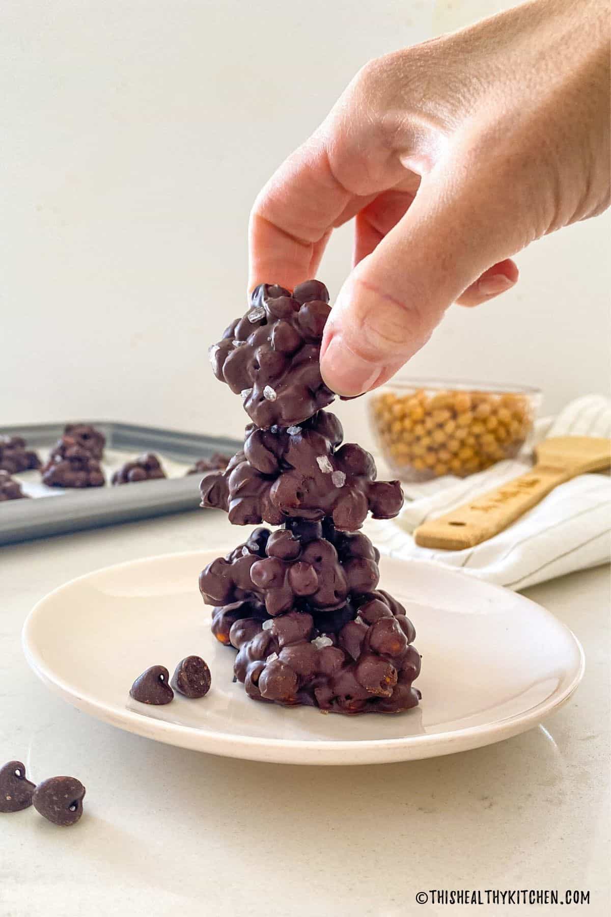Stack of chocolate-covered chickpea clusters and hand grabbing top one.