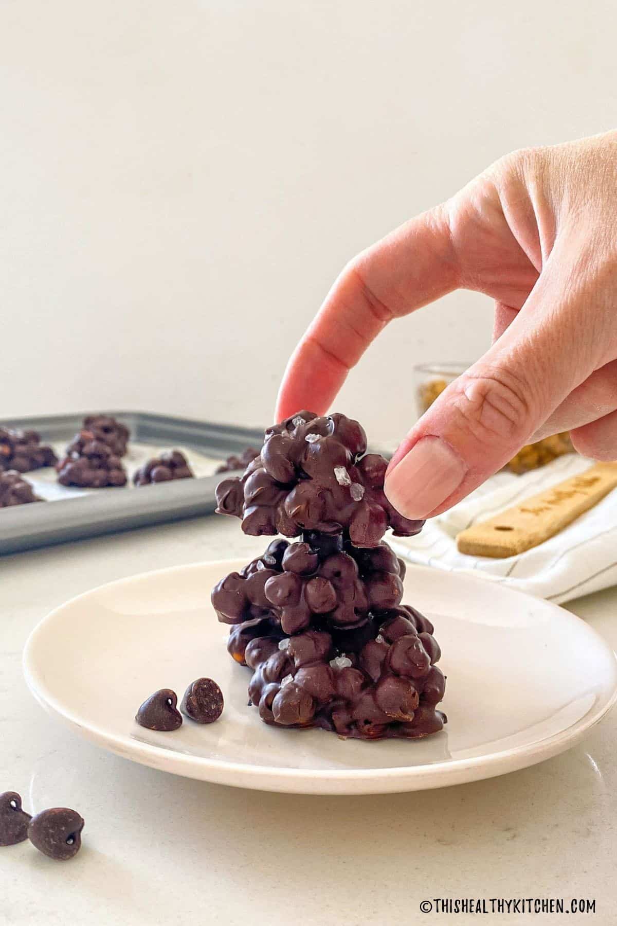 Stack of chocolate chickpea clusters and hand grabbing the top one.