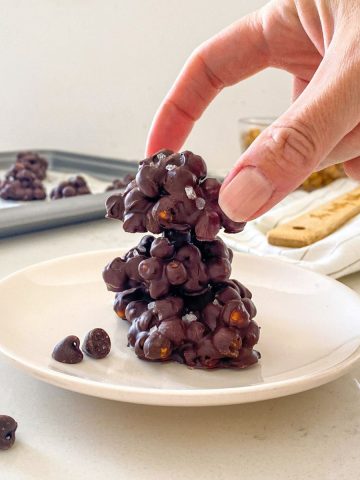 Chocolate chickpea clusters in a stack on a white plate with more in the background.