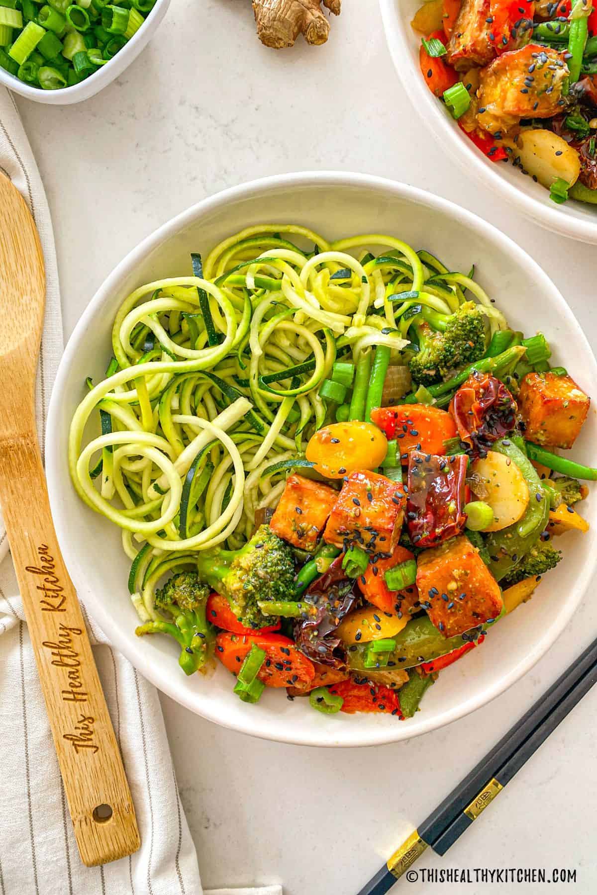 Szechuan tofu with veggies and zoodles in a white dish.