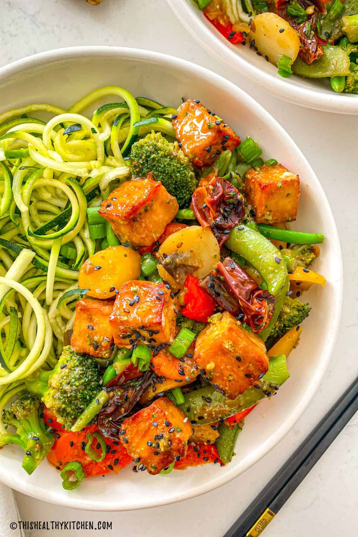 Close up of tofu cubes with broccoli, peppers, green beans, and spiralized zucchini.