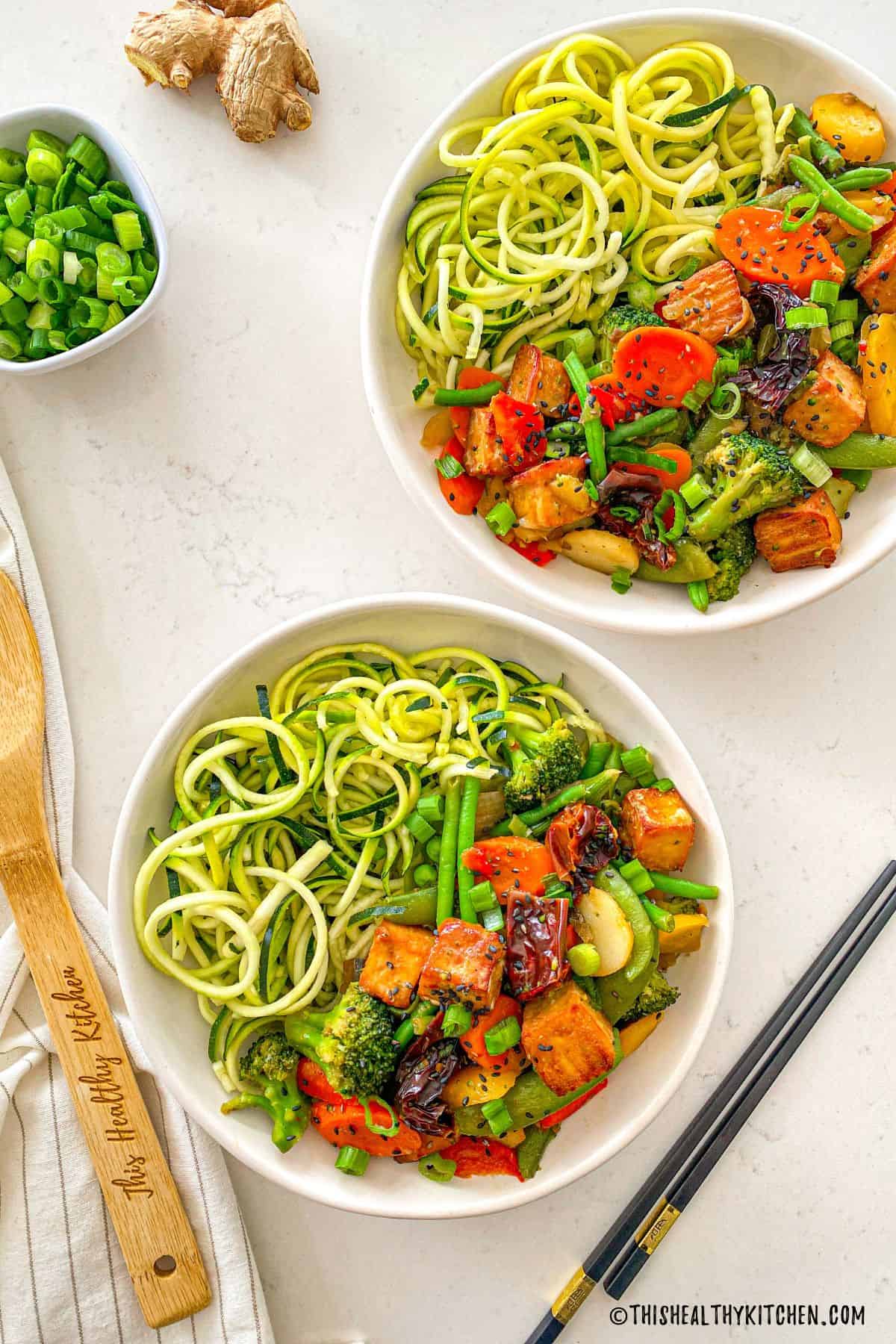 Two serving bowls filled with zucchini noodles, Szechuan tofu and veggies.