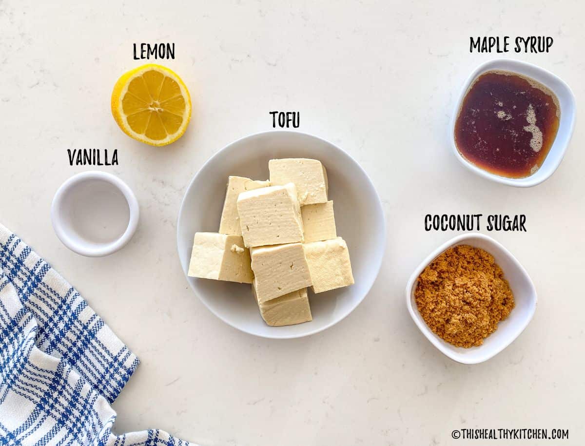 Bowl of tofu, maple syrup, coconut sugar, vanilla and half a lemon on kitchen counter.