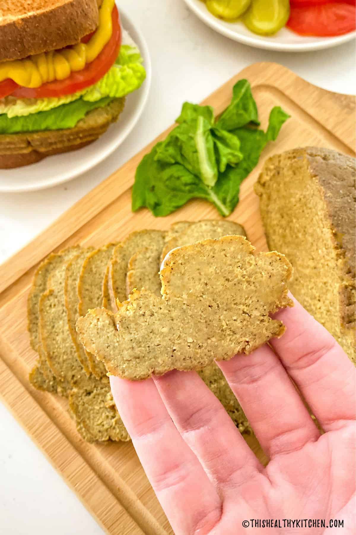 Hand holding up slice of vegan mock meat.