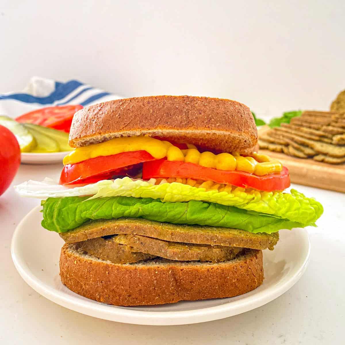 Sandwich with vegan deli meat, lettuce, tomato, and mustard.