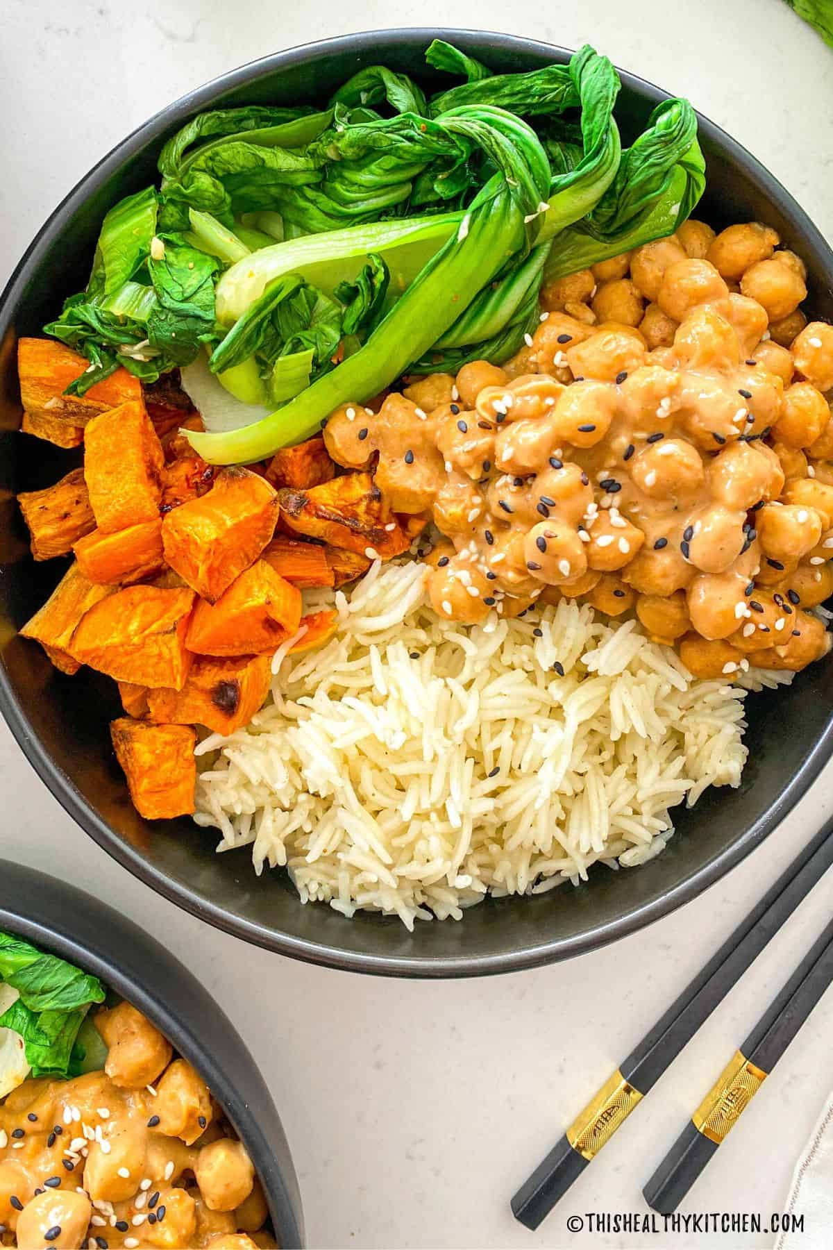 Black bowl with rice, chickpeas, bok choy and sweet potato inside.