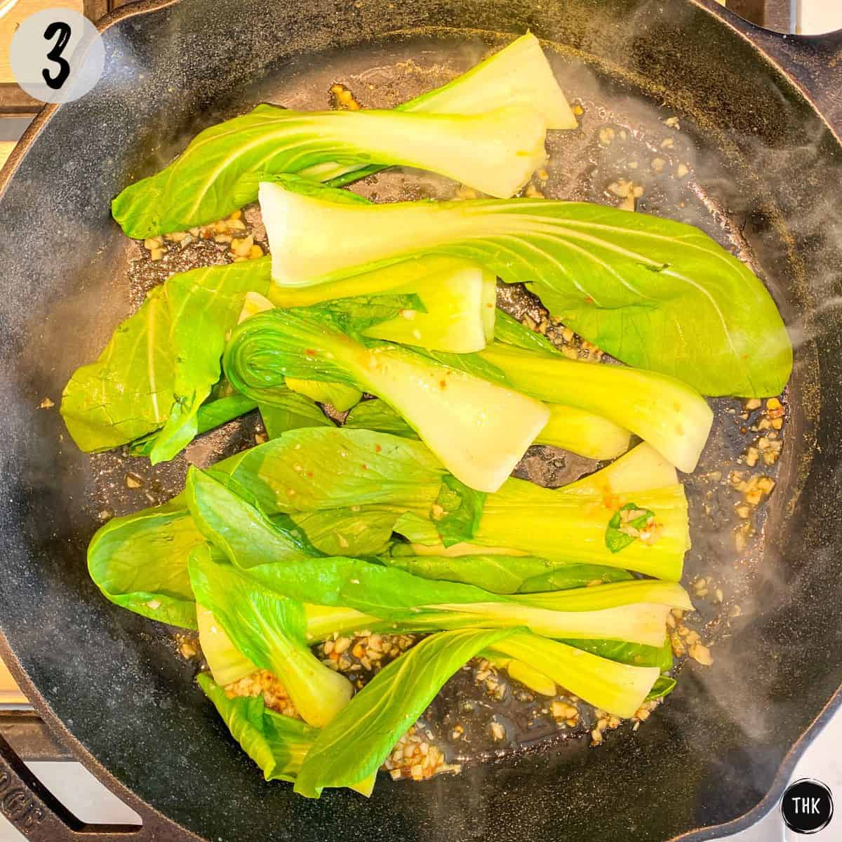 Bok choy being sautéed in cast iron pan.